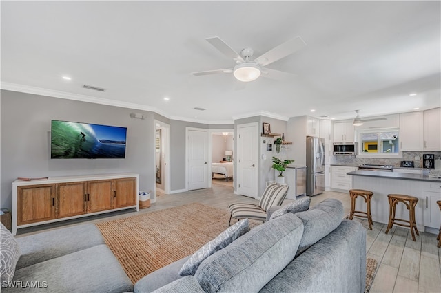 living room with ceiling fan, ornamental molding, and light wood-type flooring