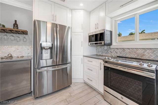 kitchen featuring appliances with stainless steel finishes, white cabinetry, decorative backsplash, light hardwood / wood-style floors, and crown molding