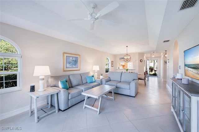 living room with a tray ceiling, ceiling fan with notable chandelier, and light tile patterned floors