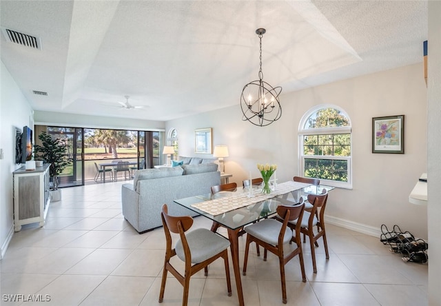 tiled dining space featuring a raised ceiling, ceiling fan with notable chandelier, and a textured ceiling