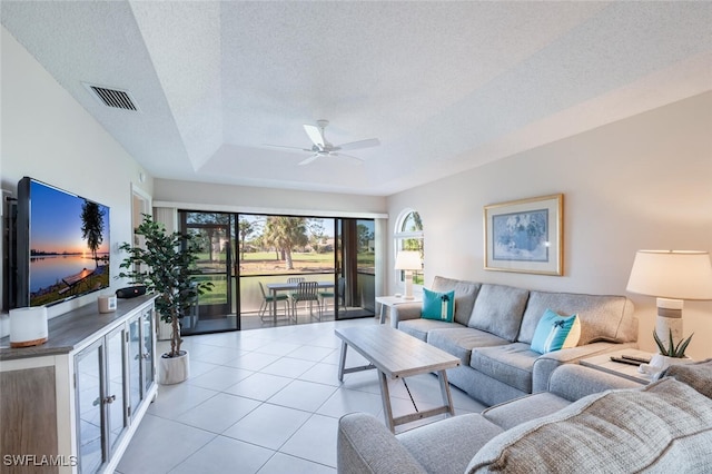 living room featuring ceiling fan, a tray ceiling, a textured ceiling, and light tile patterned flooring