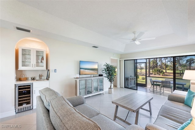 tiled living room with indoor wet bar, ceiling fan, a textured ceiling, a raised ceiling, and beverage cooler