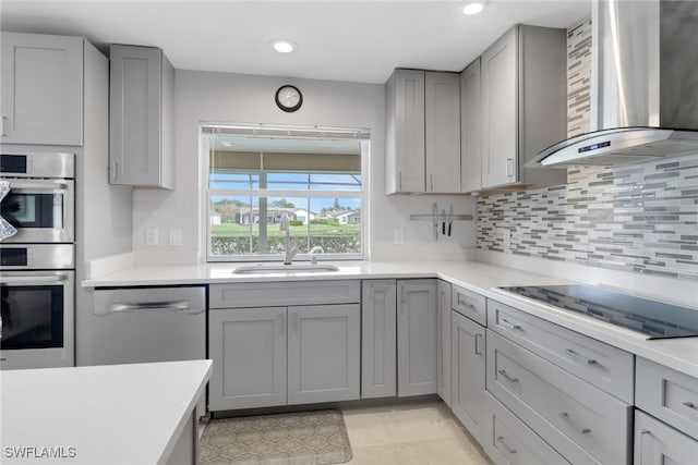 kitchen with appliances with stainless steel finishes, gray cabinets, sink, and wall chimney range hood