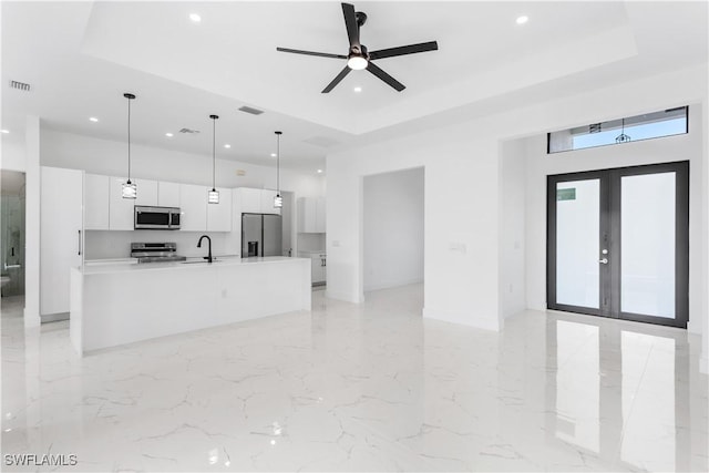 kitchen with an island with sink, white cabinetry, hanging light fixtures, stainless steel appliances, and french doors