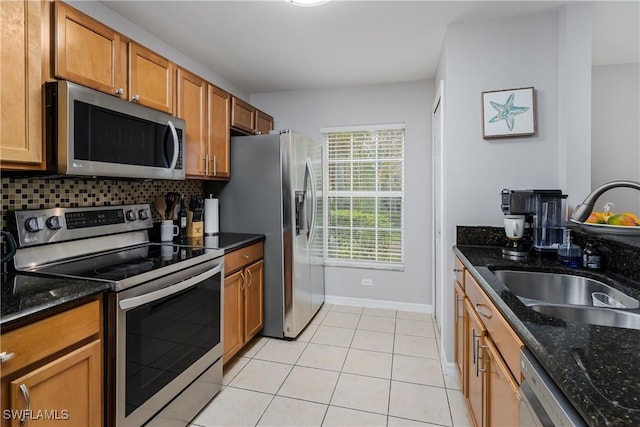 kitchen with light tile patterned flooring, stainless steel appliances, sink, and dark stone countertops