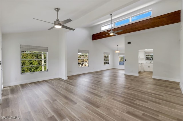 unfurnished living room with light hardwood / wood-style flooring, a towering ceiling, and ceiling fan