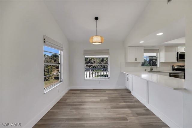 kitchen featuring vaulted ceiling, hanging light fixtures, appliances with stainless steel finishes, sink, and white cabinetry