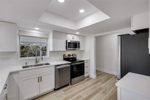 kitchen featuring light hardwood / wood-style floors, white cabinetry, sink, stainless steel appliances, and a tray ceiling