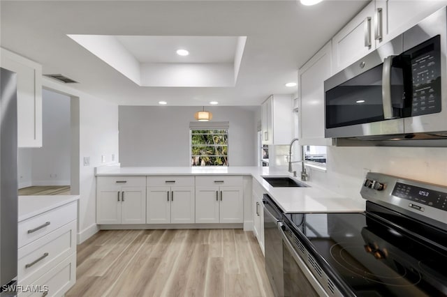 kitchen featuring white cabinets, appliances with stainless steel finishes, sink, kitchen peninsula, and a raised ceiling