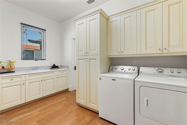 washroom featuring cabinet space, light wood finished floors, visible vents, washing machine and clothes dryer, and a sink