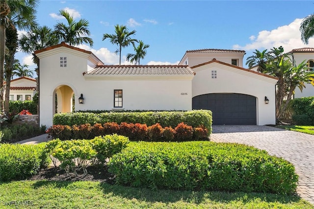 mediterranean / spanish-style house with a garage, a tile roof, decorative driveway, and stucco siding