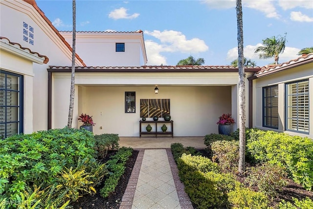 view of exterior entry with a tiled roof, a patio, and stucco siding