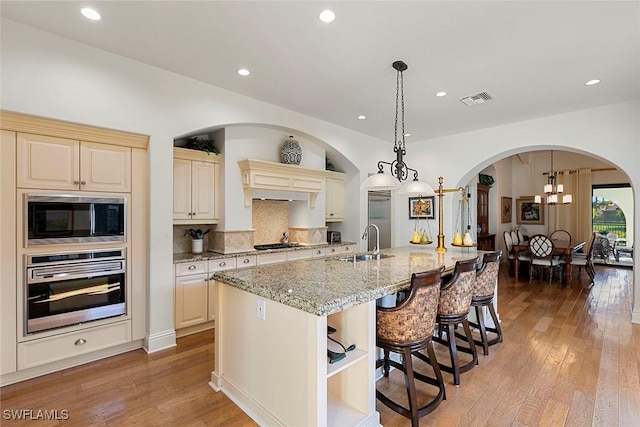 kitchen featuring a sink, visible vents, appliances with stainless steel finishes, an island with sink, and decorative light fixtures