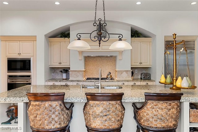 kitchen featuring stainless steel appliances, hanging light fixtures, light stone counters, and cream cabinets