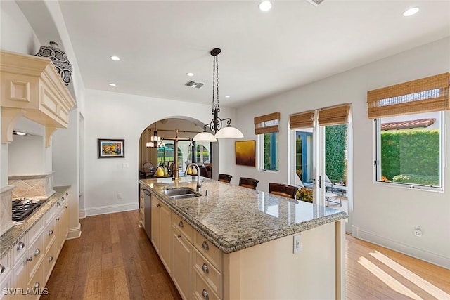 kitchen featuring decorative light fixtures, a sink, visible vents, light stone countertops, and a center island with sink