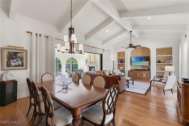 dining room featuring arched walkways, lofted ceiling with beams, light wood-style floors, built in shelves, and ceiling fan with notable chandelier