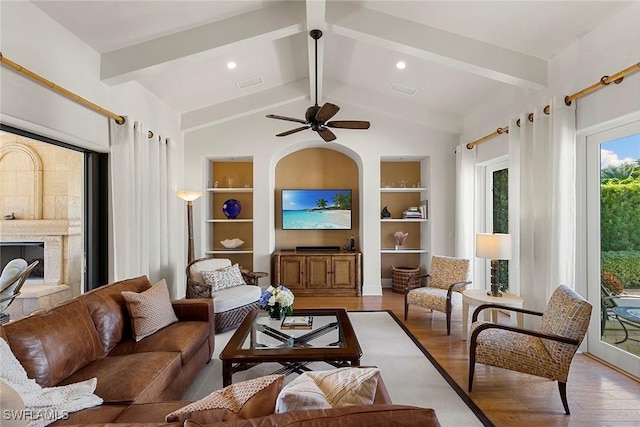 living area featuring visible vents, a fireplace with raised hearth, wood finished floors, vaulted ceiling with beams, and built in shelves