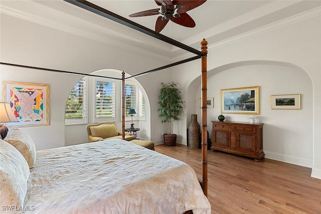 bedroom featuring arched walkways, ornamental molding, light wood-style flooring, and baseboards