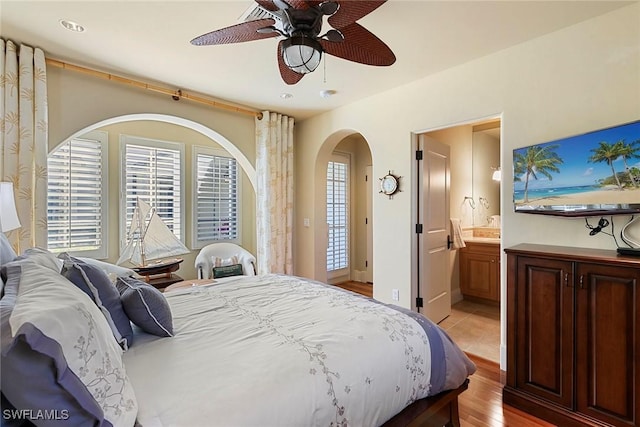 bedroom featuring ceiling fan, arched walkways, ensuite bath, and light wood-style flooring