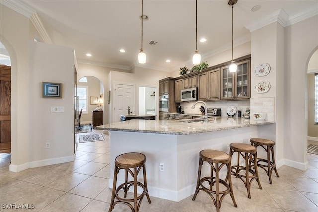 kitchen with hanging light fixtures, appliances with stainless steel finishes, light stone counters, and kitchen peninsula