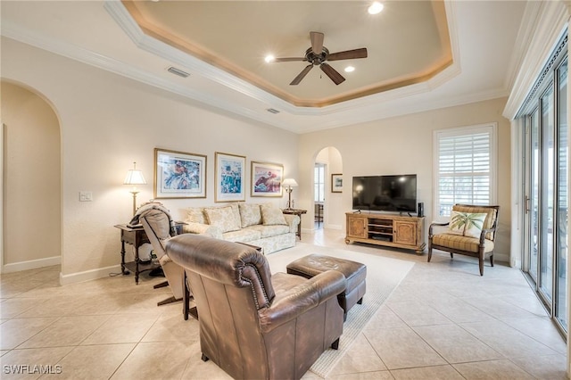 tiled living room with ceiling fan, ornamental molding, and a tray ceiling