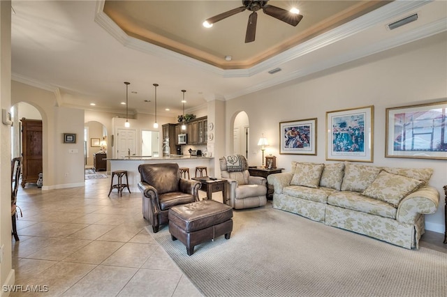 tiled living room with a tray ceiling, ornamental molding, and ceiling fan