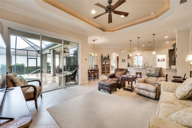 living room featuring light tile patterned flooring, crown molding, a raised ceiling, and ceiling fan with notable chandelier