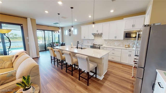 kitchen with sink, pendant lighting, stainless steel appliances, a kitchen island with sink, and white cabinets