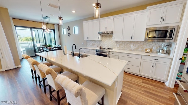 kitchen featuring appliances with stainless steel finishes, sink, white cabinets, hanging light fixtures, and a center island with sink