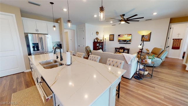 kitchen with white cabinets, stainless steel fridge, sink, and a kitchen island with sink