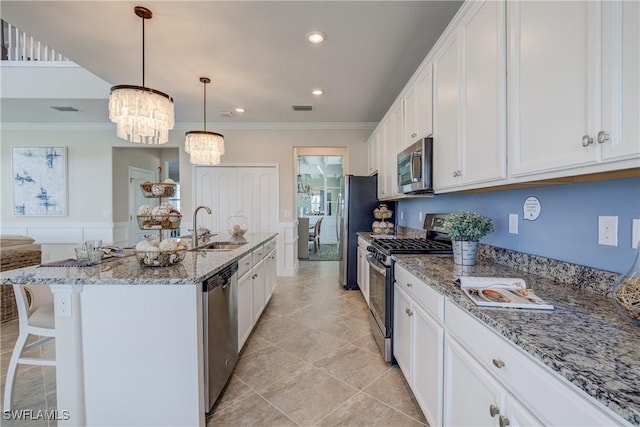 kitchen with white cabinets, appliances with stainless steel finishes, decorative light fixtures, sink, and a kitchen island with sink