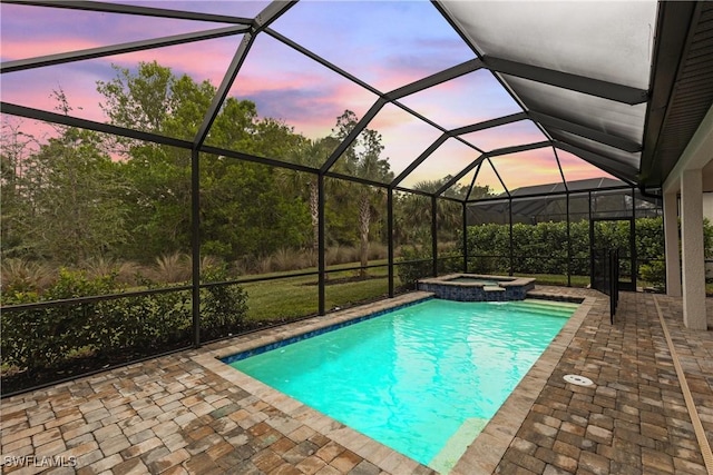 pool at dusk featuring an in ground hot tub, glass enclosure, and a patio area