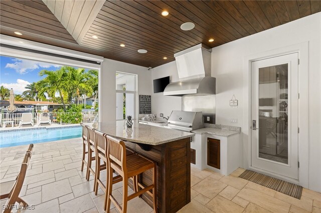 kitchen featuring ventilation hood, a kitchen bar, a center island, light stone counters, and wooden ceiling