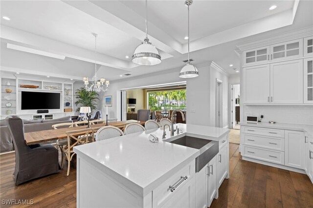 kitchen with a tray ceiling, pendant lighting, light countertops, dark wood-type flooring, and a sink