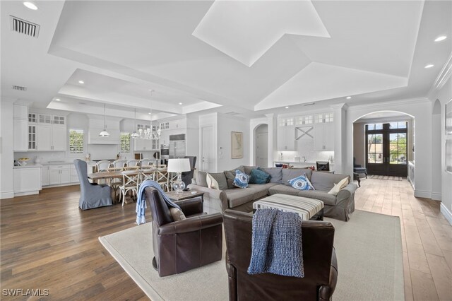 living room with an inviting chandelier, dark wood-type flooring, a raised ceiling, and french doors