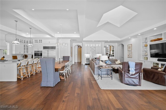 living room featuring an inviting chandelier, a tray ceiling, dark wood-type flooring, and built in features