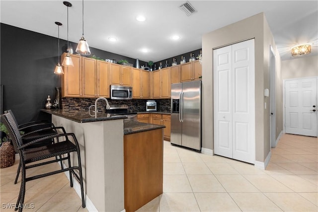 kitchen featuring pendant lighting, stainless steel appliances, dark stone counters, kitchen peninsula, and light tile patterned flooring