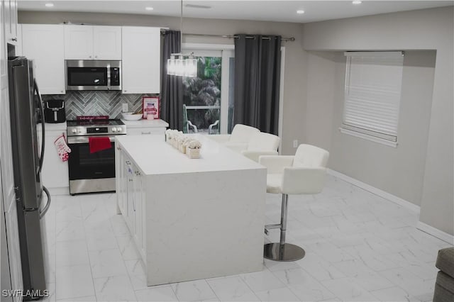 kitchen featuring white cabinetry, a center island, appliances with stainless steel finishes, pendant lighting, and backsplash