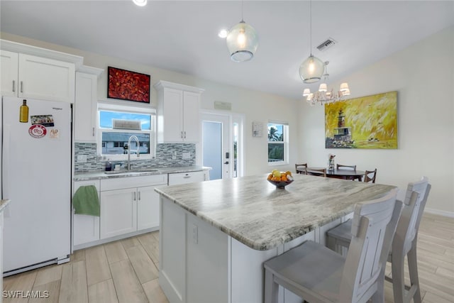 kitchen with pendant lighting, a kitchen island, white cabinetry, white fridge, and sink