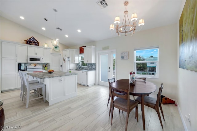 dining area featuring sink, light hardwood / wood-style floors, a chandelier, and lofted ceiling