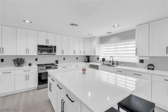 kitchen with sink, a breakfast bar area, appliances with stainless steel finishes, white cabinetry, and a center island