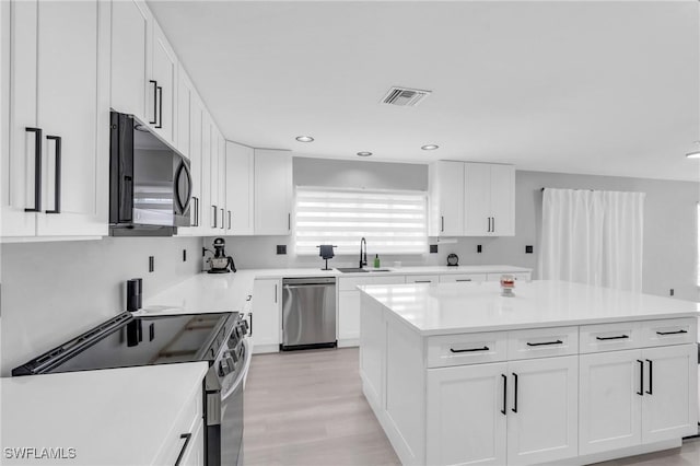 kitchen with a kitchen island, sink, white cabinets, stainless steel appliances, and light wood-type flooring