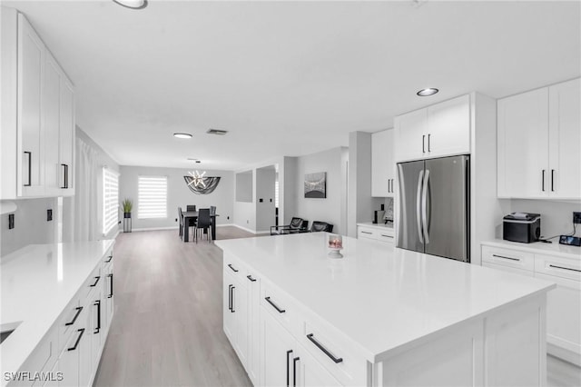 kitchen with white cabinetry, stainless steel fridge, light hardwood / wood-style flooring, and a kitchen island