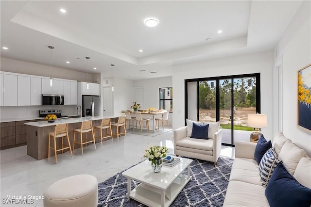 living room with a tray ceiling, recessed lighting, and light marble finish flooring