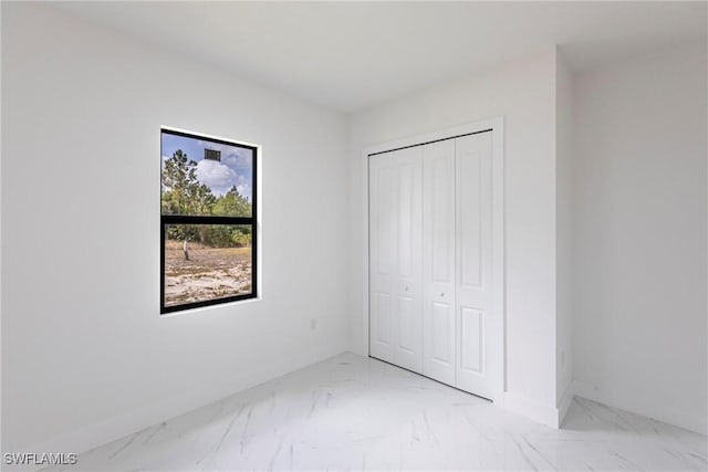 unfurnished bedroom featuring light marble finish floors, baseboards, and a closet