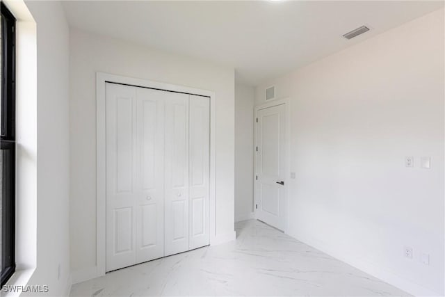 unfurnished bedroom with marble look tiles, baseboards, and a closet