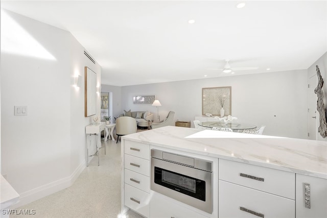 kitchen featuring white cabinetry, stainless steel microwave, ceiling fan, and light stone counters