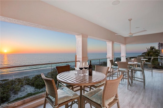 interior space with a water view, ceiling fan, decorative columns, and hardwood / wood-style flooring