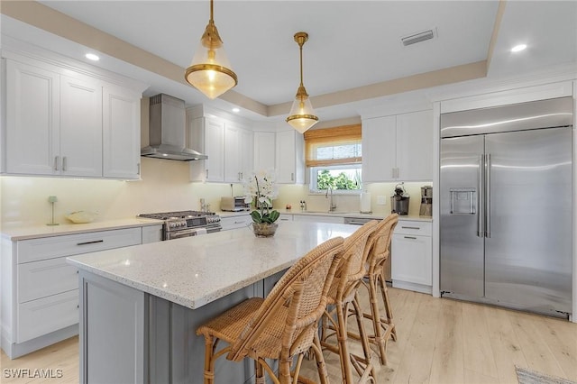 kitchen featuring white cabinetry, pendant lighting, wall chimney exhaust hood, and premium appliances