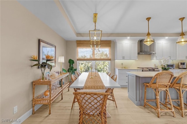 kitchen featuring wall chimney range hood, hanging light fixtures, a kitchen island, white cabinets, and a kitchen bar